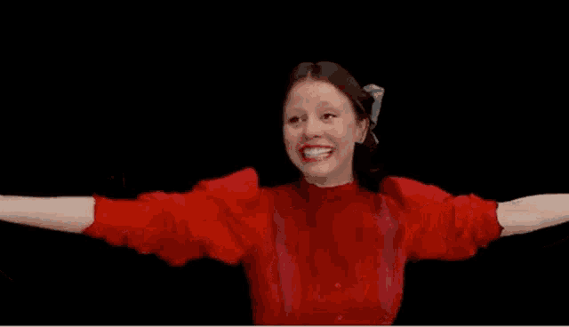 a woman in a red sweater is laughing with her arms outstretched in front of a black background .