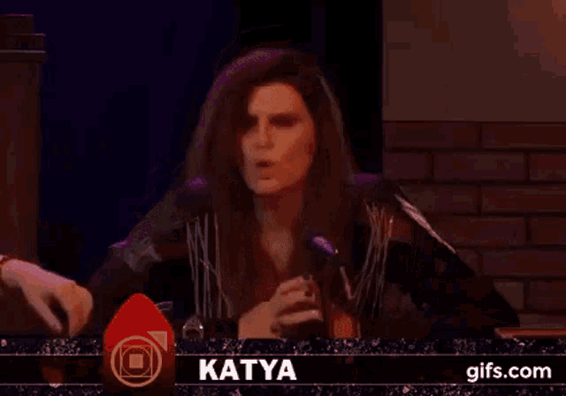 a woman is sitting at a table with her arms outstretched in front of a microphone in a dark room .