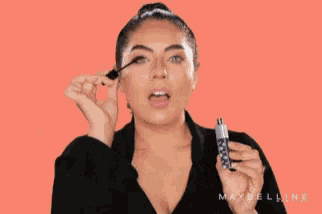 a woman is holding a bottle of maybelline mascara and making a face .