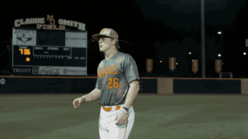 a baseball player with the number 26 on his jersey stands in front of a scoreboard