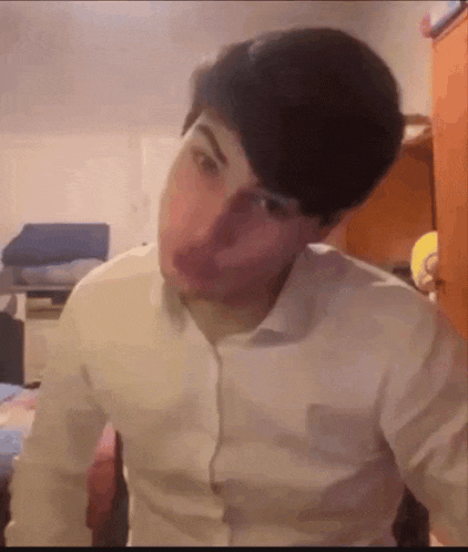 a man in a white shirt is making a funny face while sitting in a room .