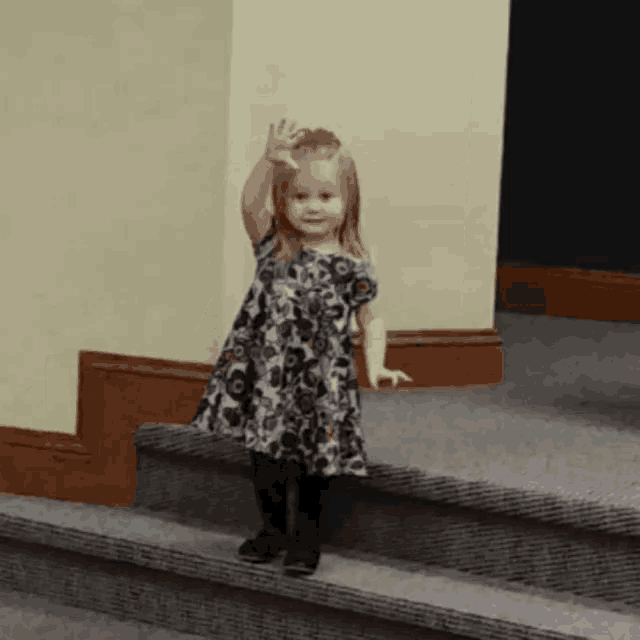a little girl in a dress is standing on a set of stairs waving her hand