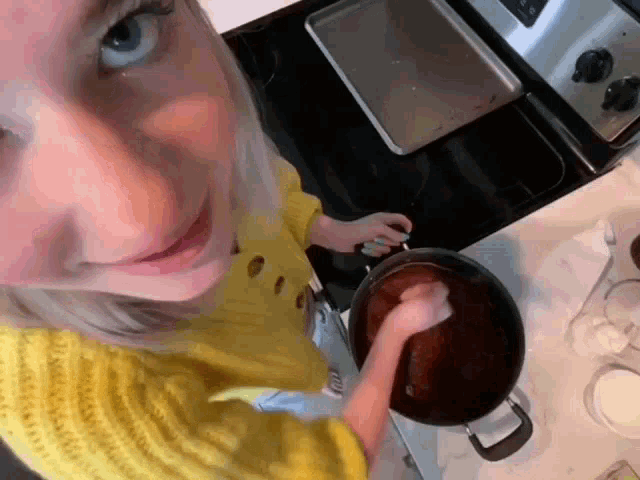 a woman in a yellow sweater is stirring a pot on a stove