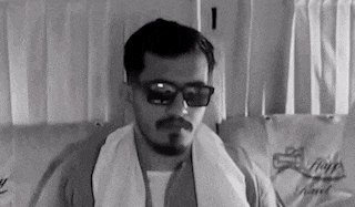 a man with a beard and mustache wearing sunglasses and a towel around his neck .