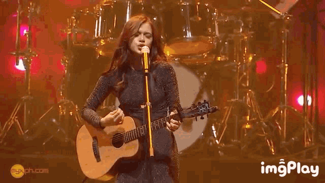a woman is playing a guitar and singing into a microphone .