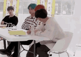 a group of young men are sitting at a table and one of them is wearing a sweater that says l.
