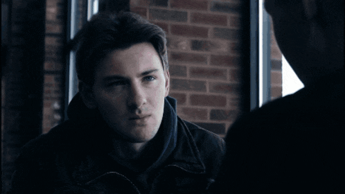 a man in a black jacket is talking to another man and the word what is on the screen