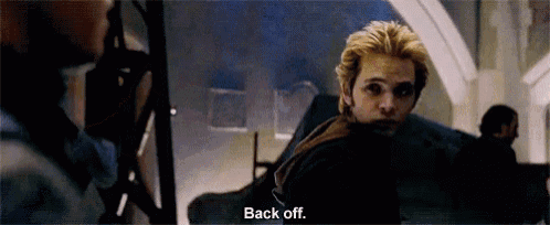 a man with blonde hair is standing in a dark room and talking to another man .
