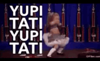 a little girl is dancing in front of trophies and the words yupi tati yupi tati are on the screen .