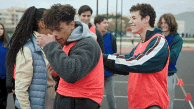 a group of young people are standing on a basketball court and one of them is touching another 's face