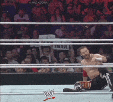 a wrestler in a wrestling ring holds a sign that says believe