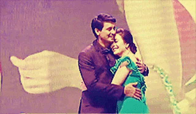 a man in a suit and a woman in a green dress hugging each other