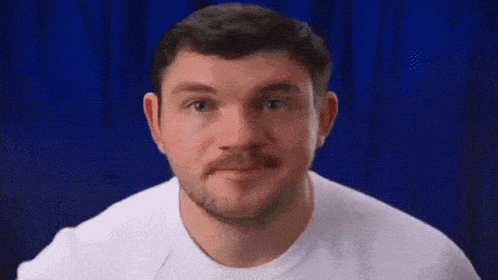 a man with a beard and mustache is wearing a white t-shirt and making a funny face .