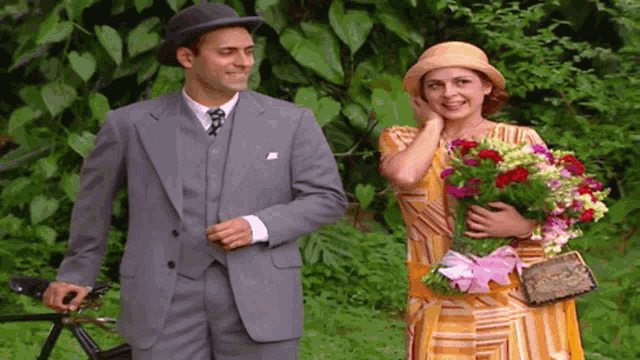 a man in a suit holds a bicycle while a woman in a hat holds flowers