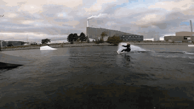 a person riding a wakeboard in a lake with a smokestack in the background