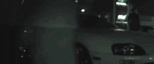 a car is driving down a street at night and a person is standing in front of it .