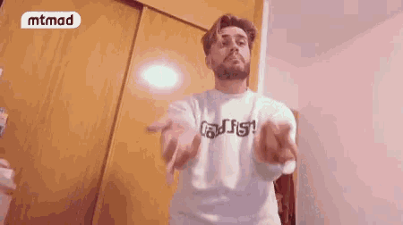 a man in a white sweatshirt giving the middle finger with a mtmad logo behind him