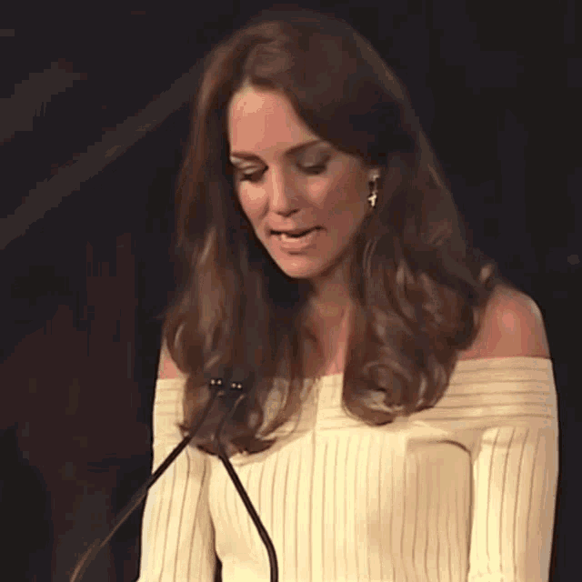 a woman wearing a white off the shoulder top stands in front of a microphone