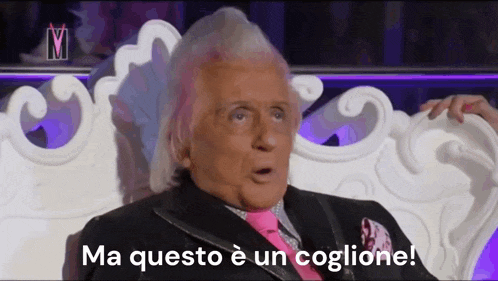 a man in a suit and pink tie is sitting in a chair with the words ma questo e un coglione written below him .
