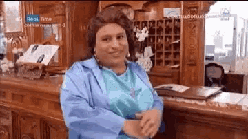 a woman in a blue jacket and wig is sitting at a hotel counter .