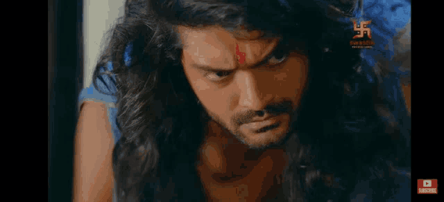 a man with long hair and a beard is looking at the camera with a red bindi on his forehead .