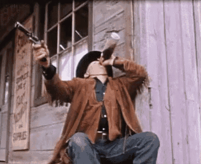 a man in a cowboy hat is drinking from a glass while holding a gun in front of a building .