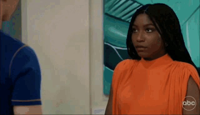 a woman in an orange top is looking at a man in a blue shirt on abc
