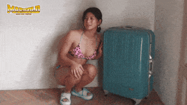 a woman in a bikini squatting next to a suitcase that says madman on the bottom