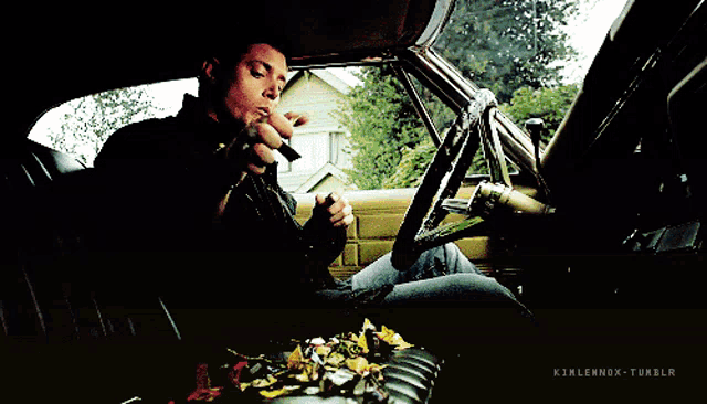 a man is sitting in the driver 's seat of a car with a bunch of leaves on the floor