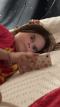 a little girl is laying on a bed looking at her cell phone