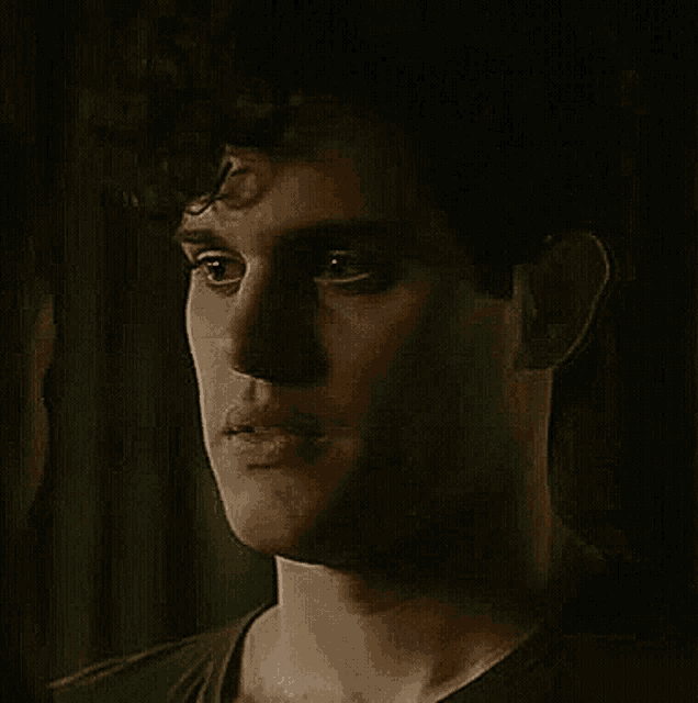 a close up of a man 's face with curly hair and a black shirt .