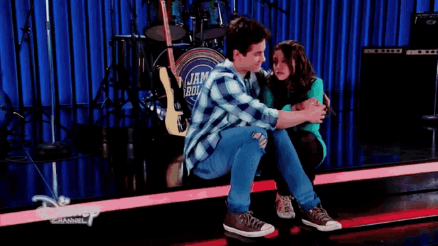 a boy and a girl are hugging on a stage with a drum set in the background that says jam & roller