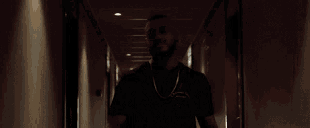 a man with a beard and a chain is walking down a dark hallway .
