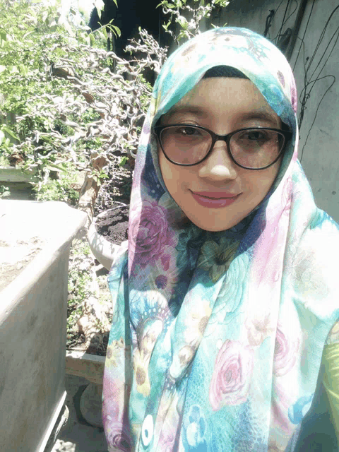 a woman wearing glasses and a floral scarf looks at the camera