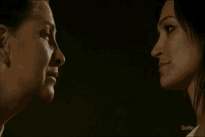 two women are looking at each other in a dark room with the word sofi on the bottom right corner .