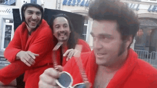 a man in a red robe holds a pair of sunglasses in front of two other men