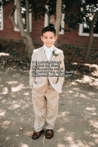 a young boy in a suit stands in front of trees