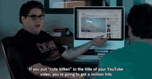 a man in a delaware shirt is talking to another man in front of a computer