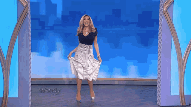 a woman in a striped skirt is standing in front of a blue wall that says wendy on it