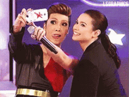 two women are taking a selfie with a cell phone and the words lscdaduos are on the bottom right