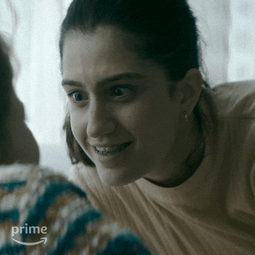 a woman with braces on her teeth looks at another woman 's face with a prime arrow in the corner