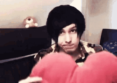 a young man with black hair is holding a red heart shaped pillow .