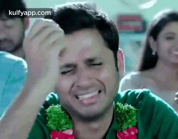 a man is laughing while holding his hand to his forehead in front of a group of people .