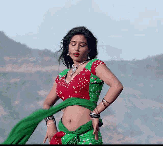 a woman in a red and green outfit is dancing in front of mountains