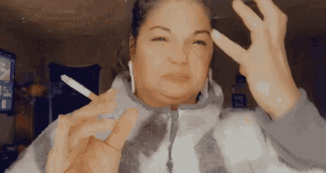 a woman is smoking a cigarette and making a peace sign with her hands .