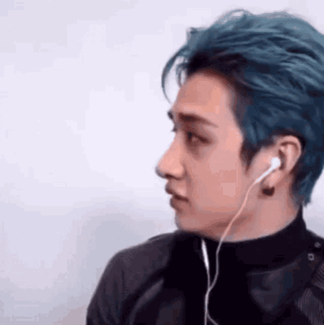 a man with blue hair is wearing headphones and a black jacket .