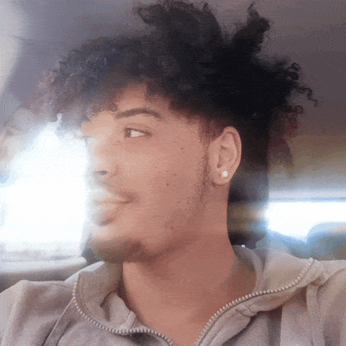 a young man with curly hair wearing a grey hoodie