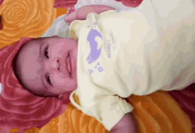 a baby wearing a yellow shirt with an elephant on it is laying on a blanket