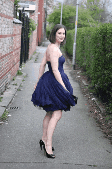 a woman in a blue dress and black heels is standing on a sidewalk