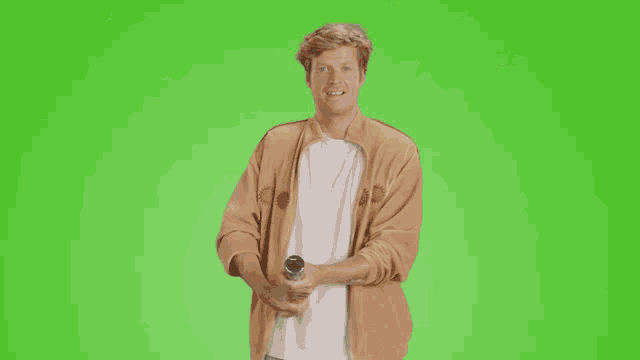 a man in a brown jacket is holding a bottle of orange soda with a green screen behind him